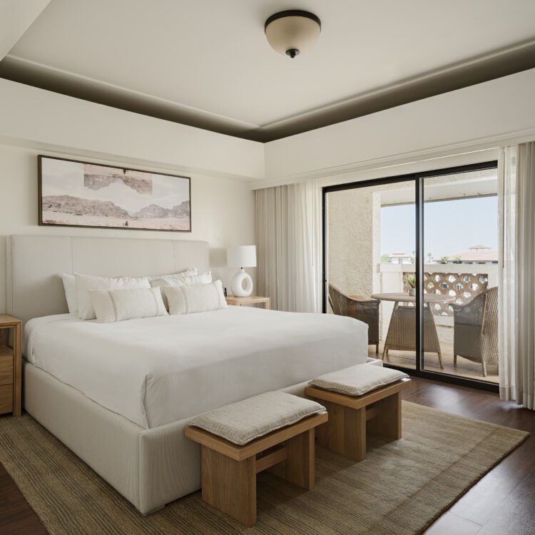 Modern master bedroom in the Mountainside Grand Suite featuring a king-size bed, bedside tables with lamps, a private balcony with seating, and floor-to-ceiling curtains.